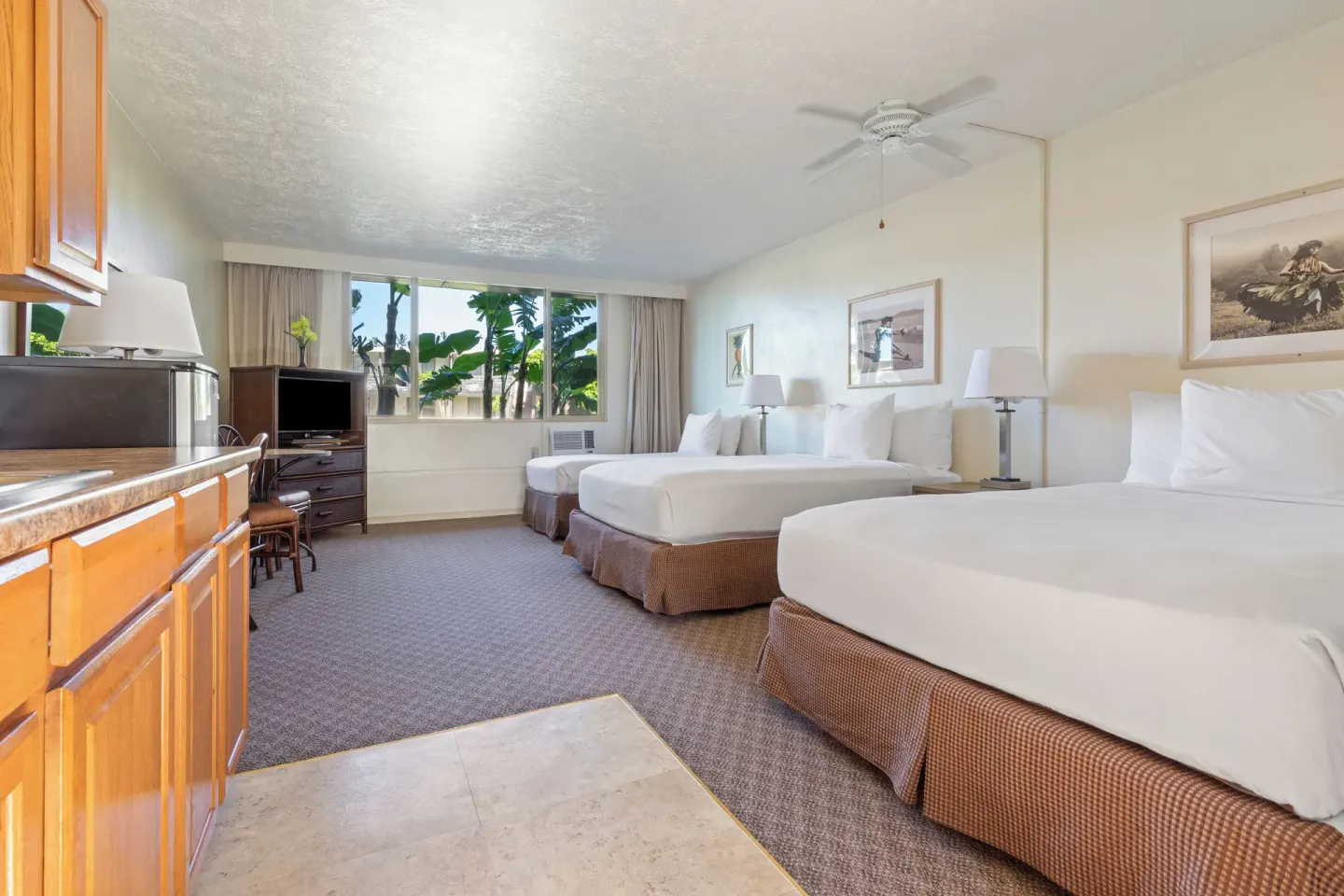 Guest room with three beds, kitchenette, desk, and window at Maui Seaside Hotel.