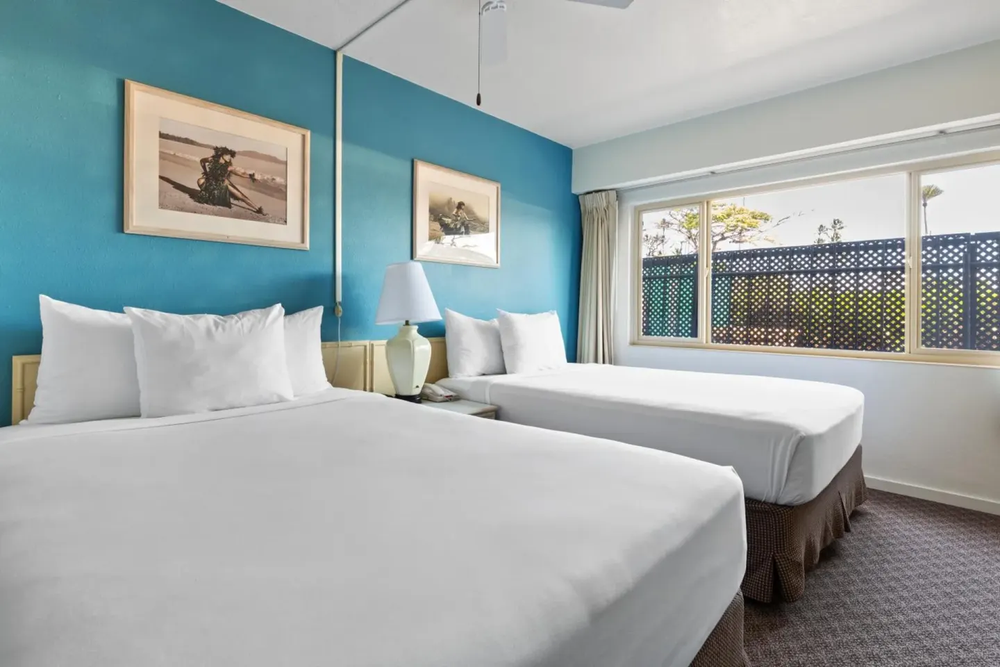 Two-bed guest room with blue accent wall and large window at Maui Seaside Hotel.