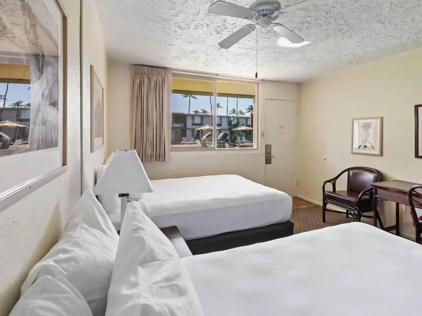 Guest room with two beds, desk, chair, and window overlooking the courtyard at Maui Seaside Hotel.
