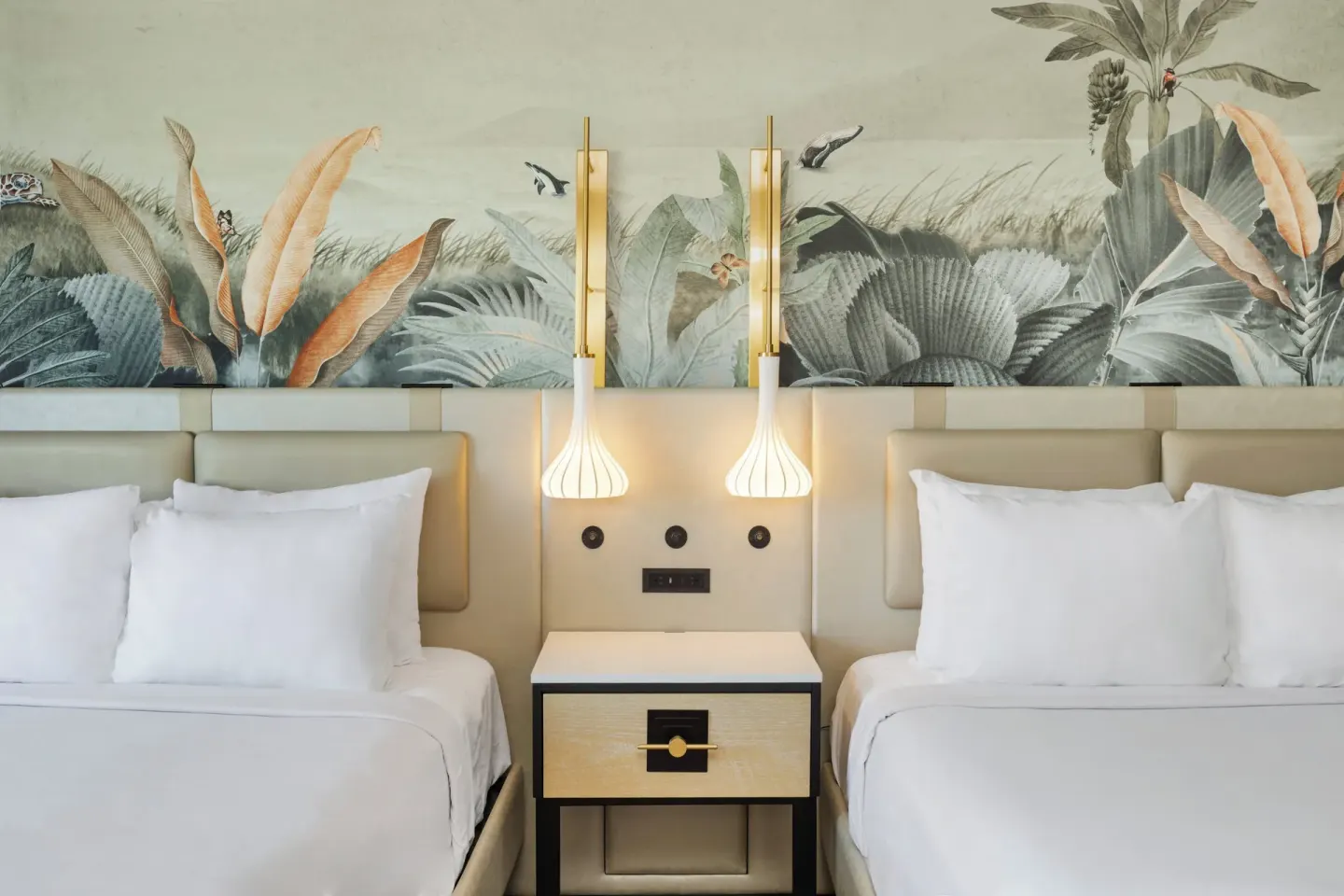 Two beds with tropical mural headboard and pendant lights at Maui Seaside Hotel.