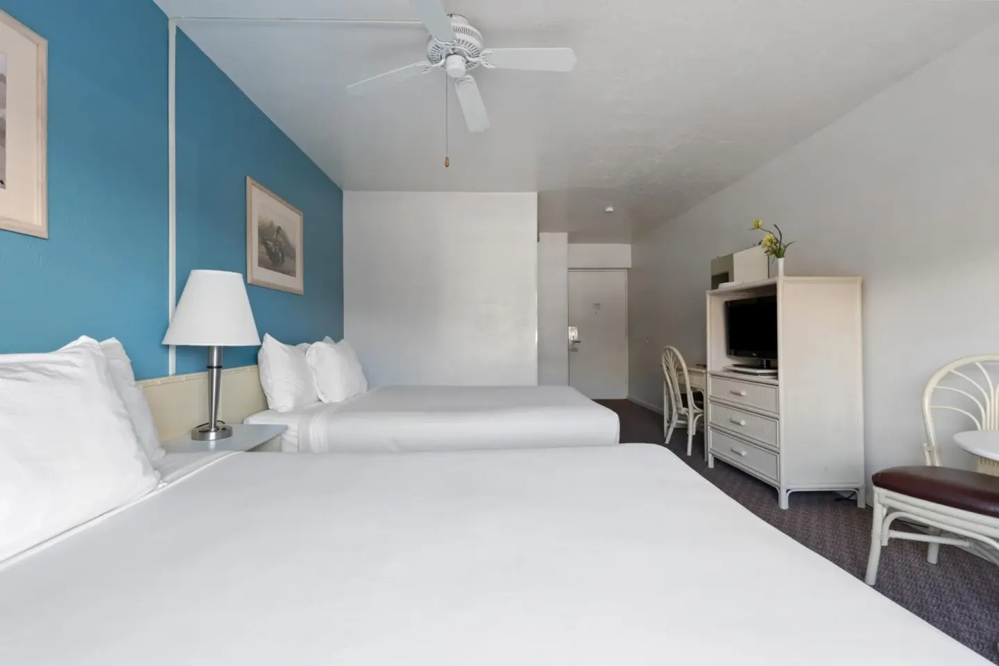 Two-bed guest room with blue wall, TV cabinet, and small dining table at Maui Seaside Hotel.