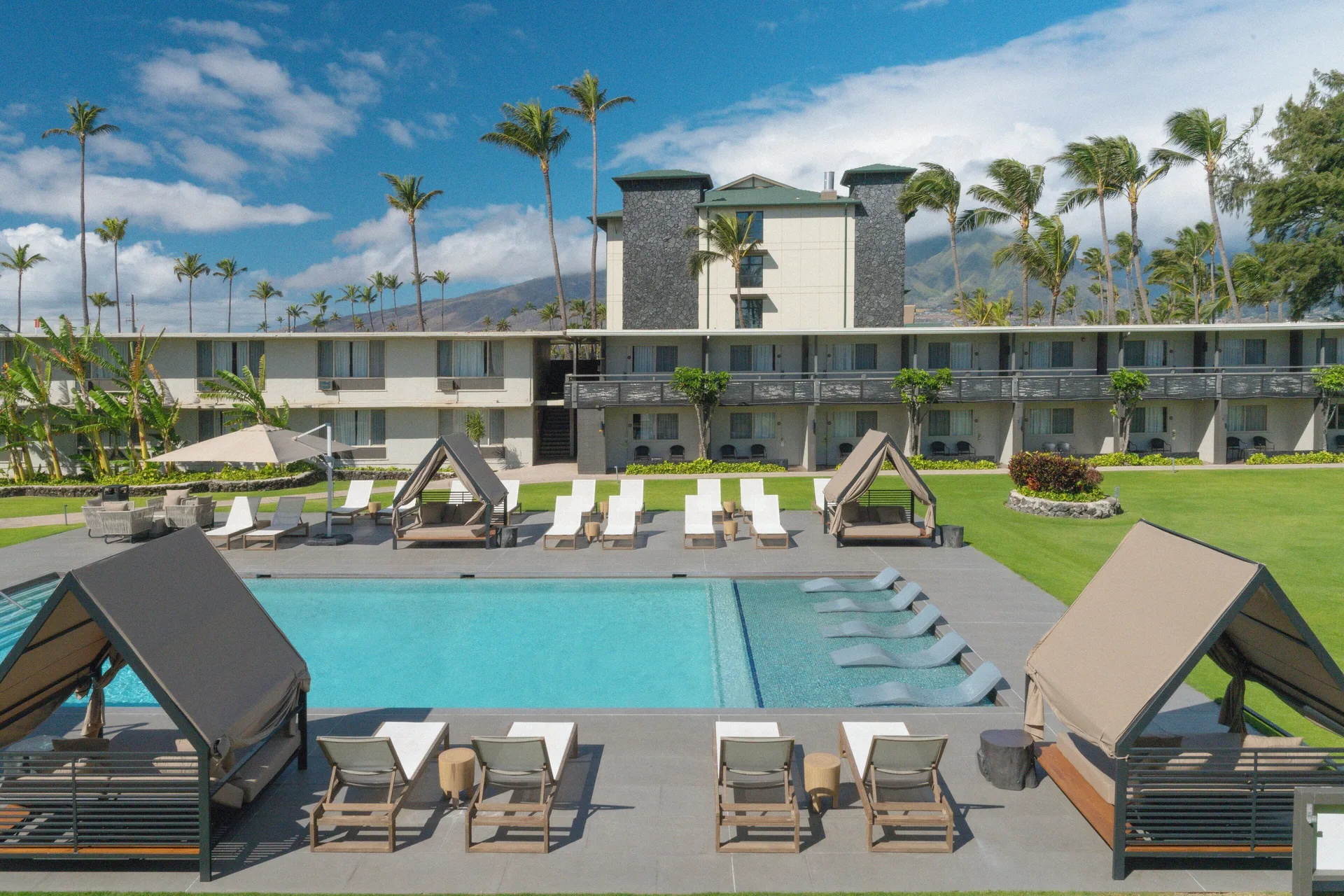 Pool courtyard with cabanas, loungers, palms, and guest room buildings at Maui Seaside Hotel.