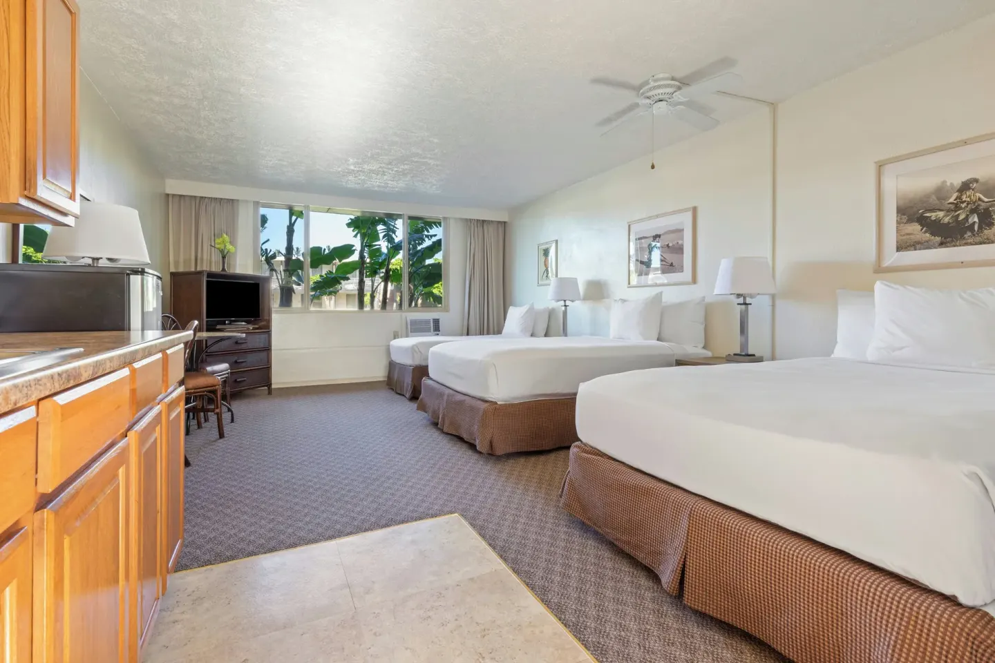 Poolside room with three beds, kitchenette, TV, and window greenery at Maui Seaside Hotel.