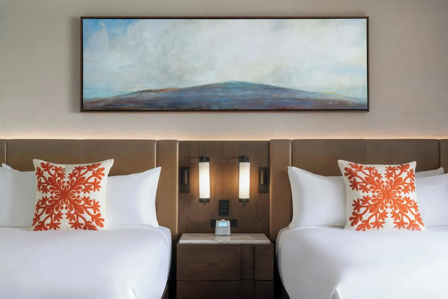 Two beds with orange accent pillows in a Deluxe Golf View Tower room at Mauna Kea Beach Hotel.