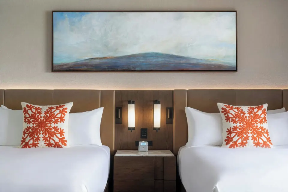 Two beds with orange accent pillows in a Deluxe Golf View Tower room at Mauna Kea Beach Hotel.