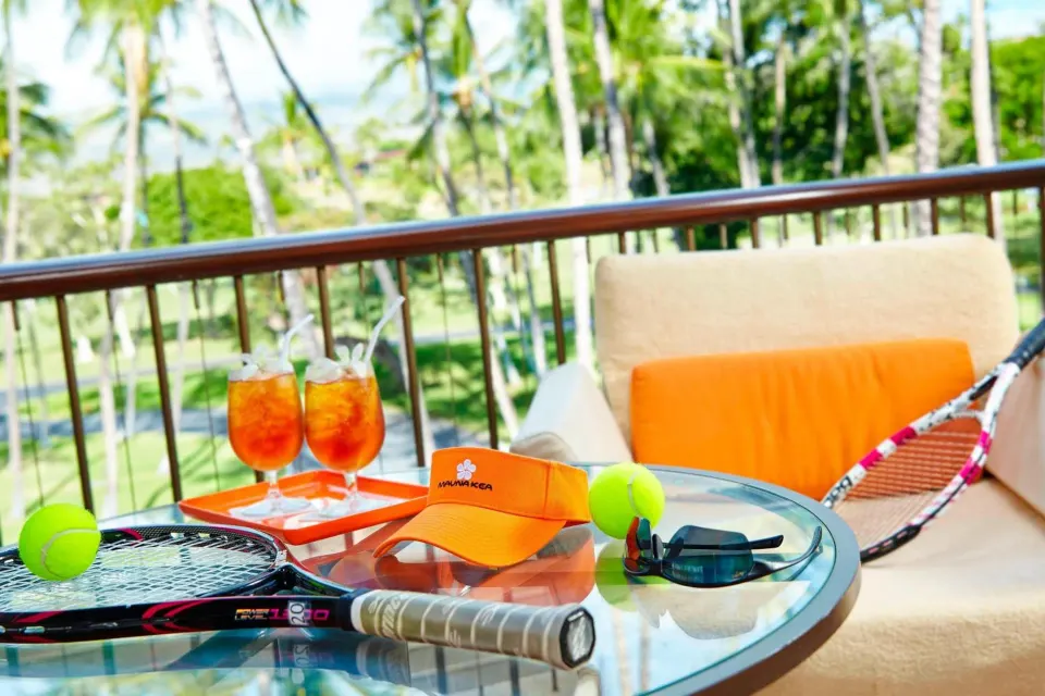 Balcony table with tennis gear, drinks, and palm views at Mauna Kea Beach Hotel.