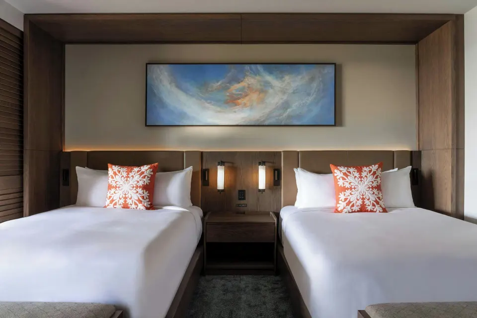Two-bed beachfront room with wall art and bedside lighting at Mauna Kea Beach Hotel.