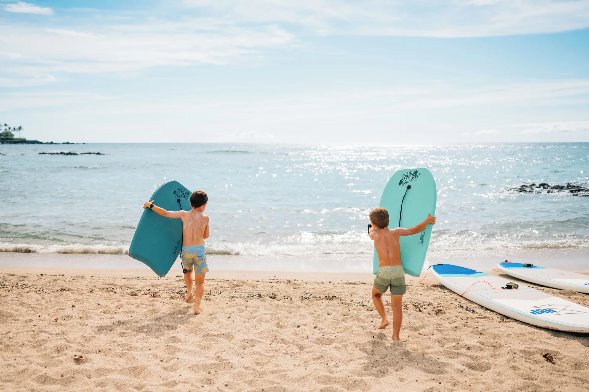 Children carry bodyboards toward the bright ocean at Mauna Lani.