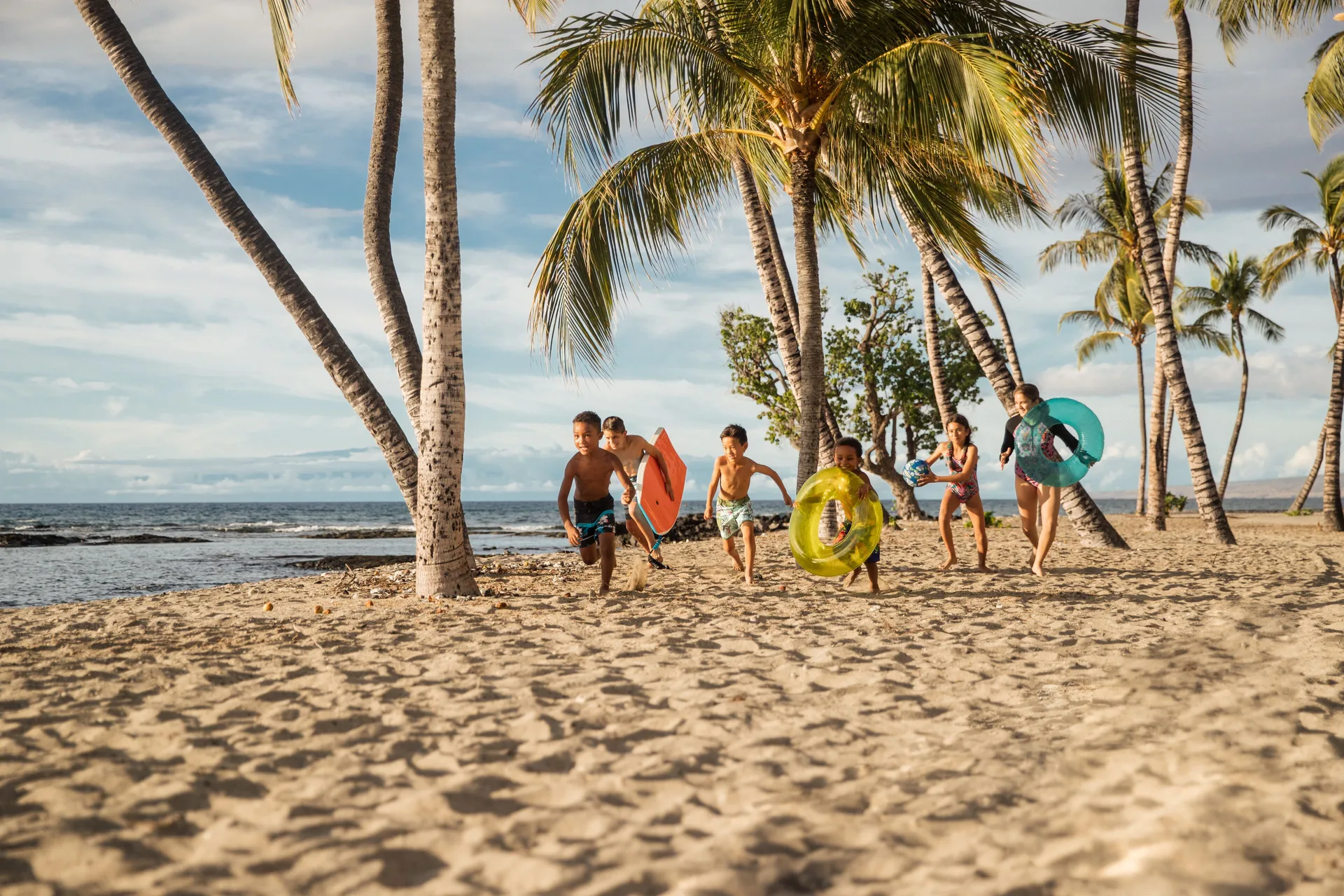 Children run with swim floats along the palm-lined beach at Mauna Lani.