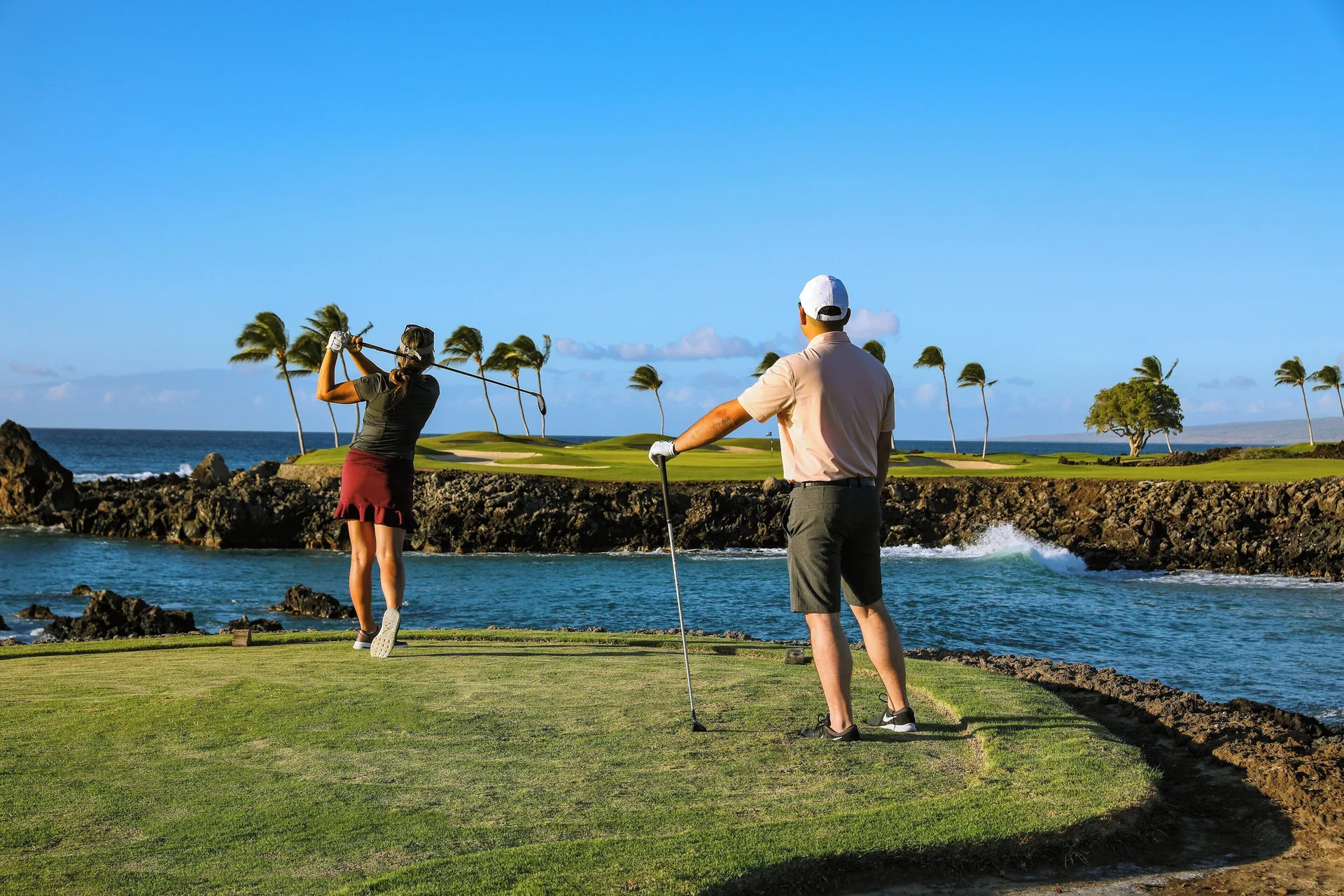 Two golfers teeing off across a coastal inlet at Mauna Lani.