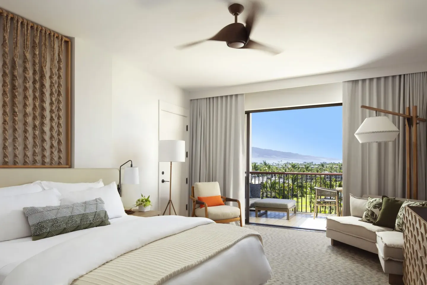 King bed guest room with sofa, balcony, and distant coastline view at Mauna Lani.