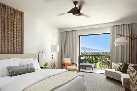 King bed guest room with sofa, balcony, and distant coastline view at Mauna Lani.