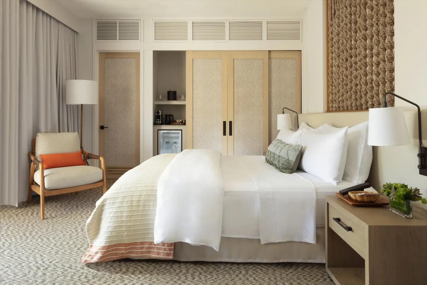 King bed guest room with lounge chair, wardrobe, and minibar nook at Mauna Lani.