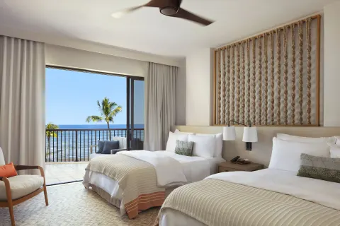 Two queen beds beside a balcony with palm trees and ocean view at Mauna Lani.