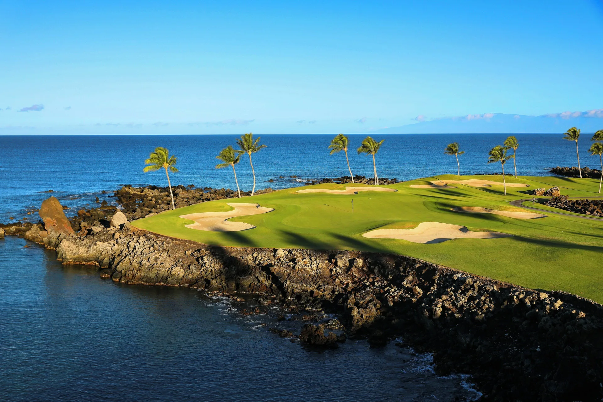 Oceanfront golf green with sand bunkers and palms at Mauna Lani.