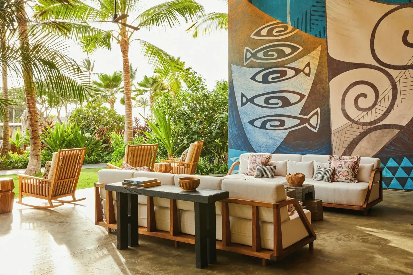 Open-air lounge with sofas, palm trees, and a fish mural at Mauna Lani.