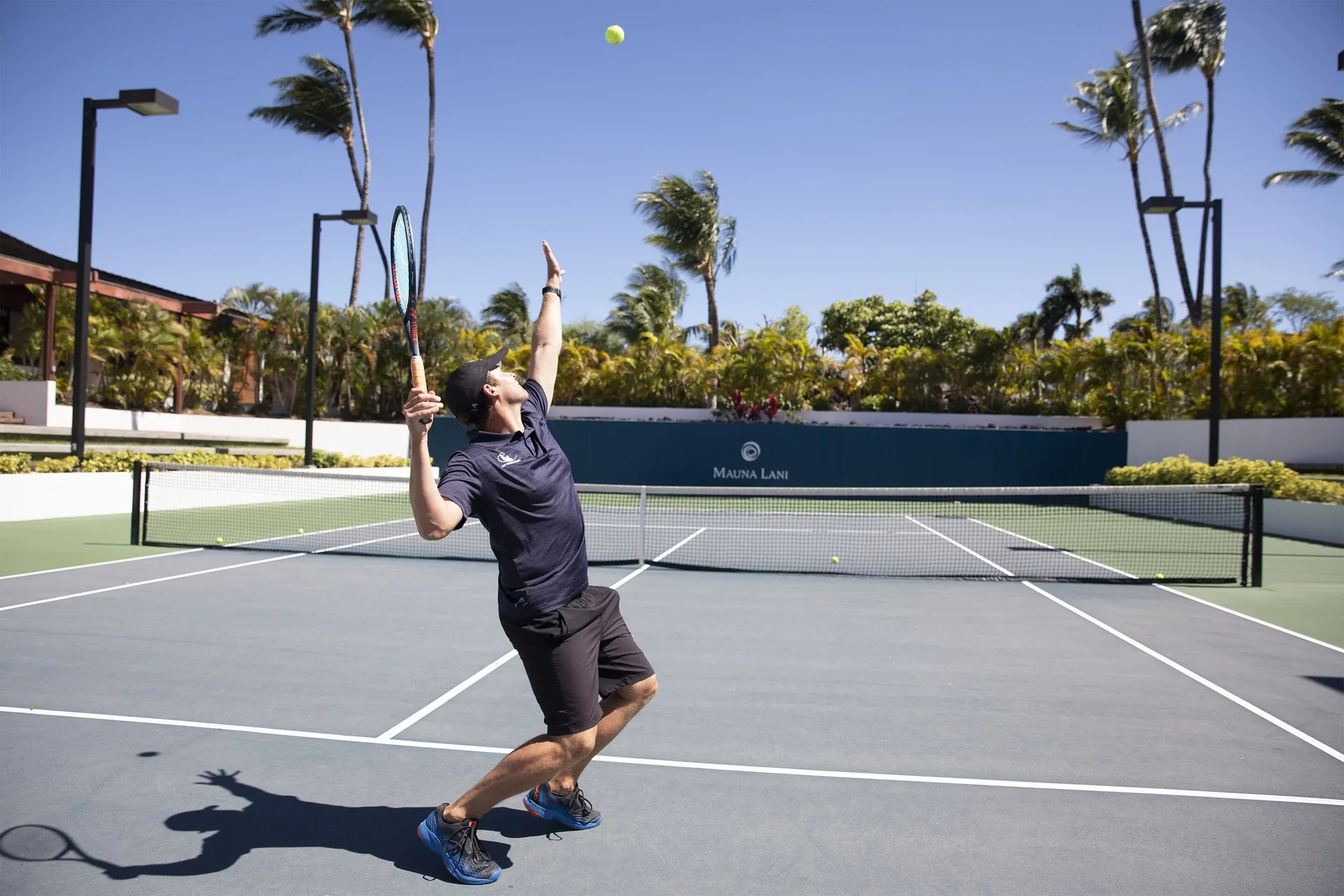 Tennis player serving on a palm-lined court at Mauna Lani.
