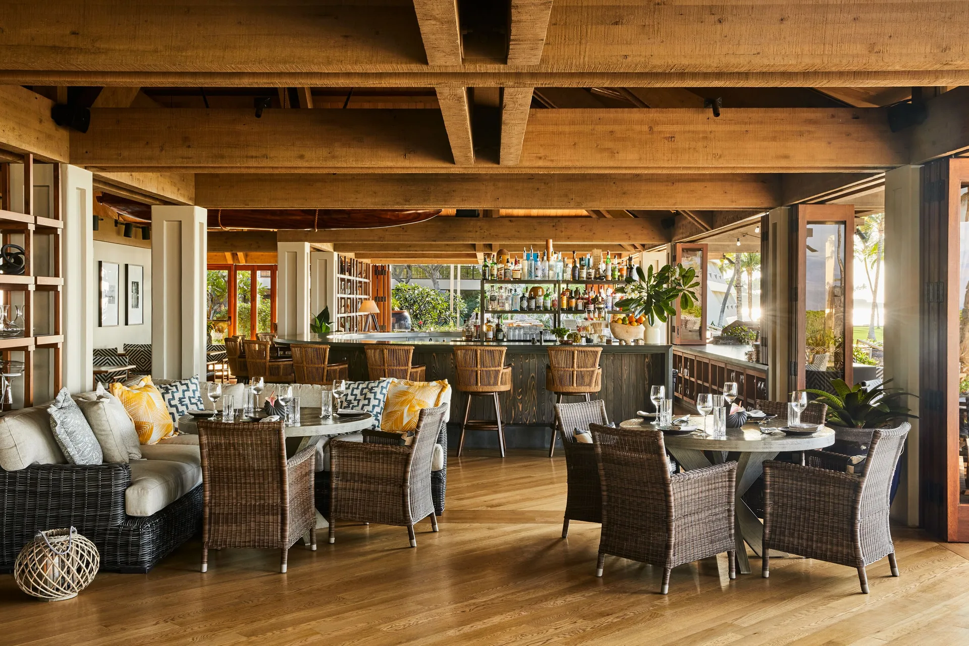An open-air dining room and bar with wicker seating are set for service at Mauna Lani.