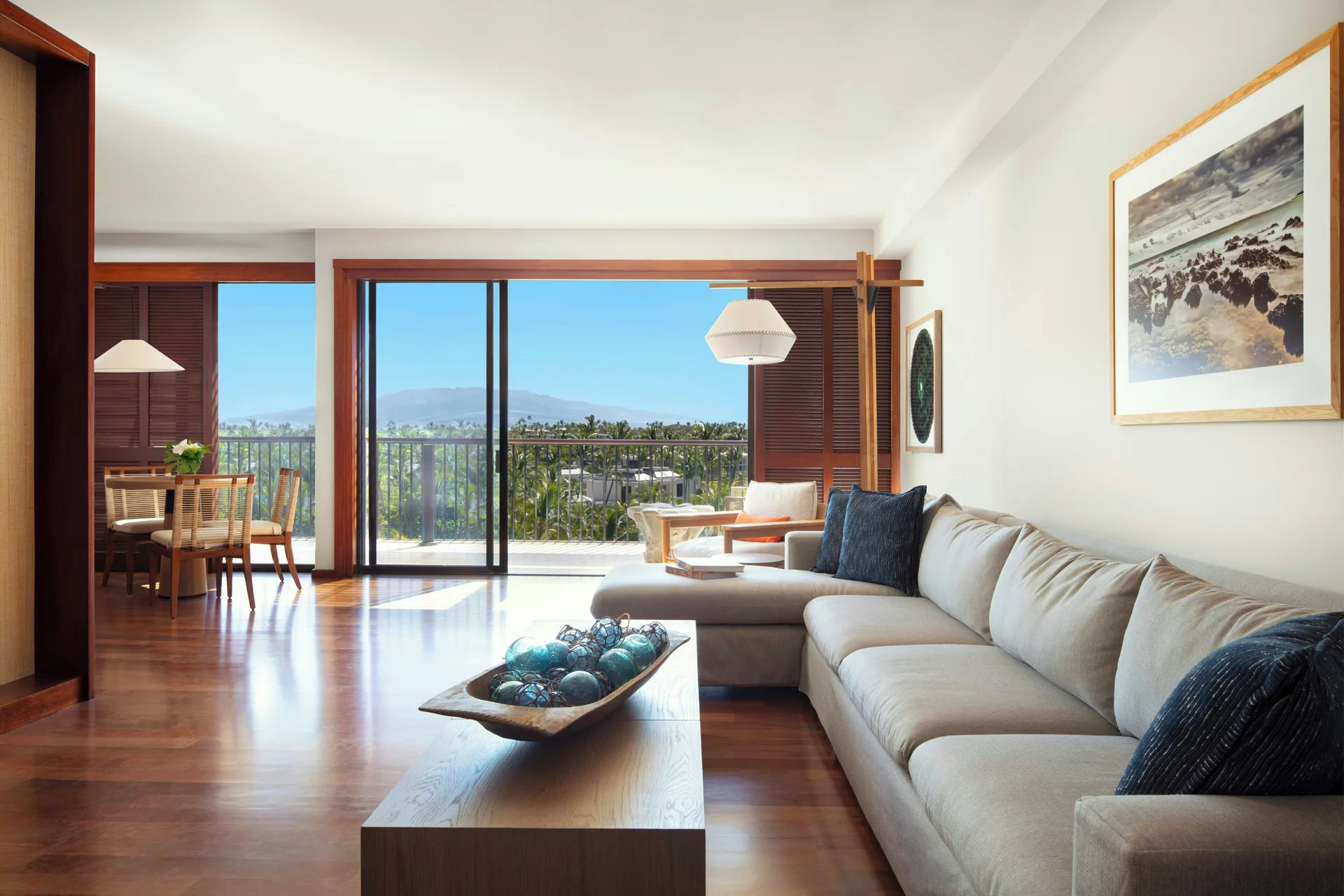 Living room with sofa, dining table, balcony, and ocean view in a Deluxe Suite at Mauna Lani.