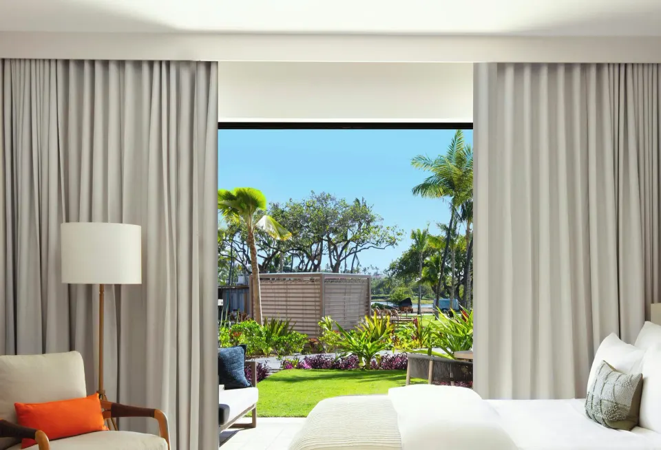 Garden View room detail at Mauna Lani looking past the bed and chair to palms and lawn outside.