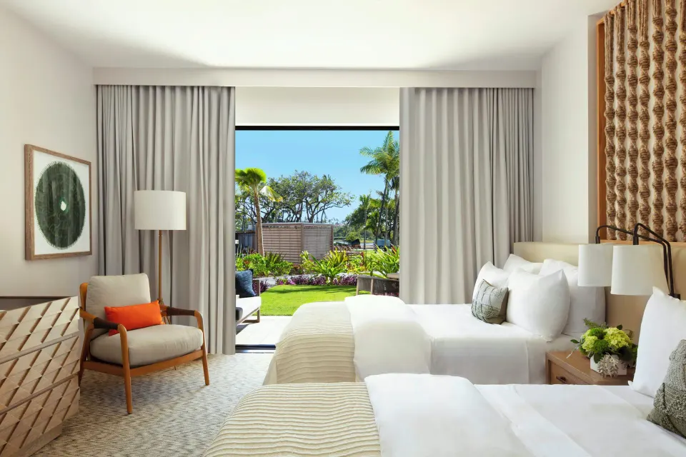 Garden View room at Mauna Lani with two beds, an armchair, and greenery outside the glass doors.