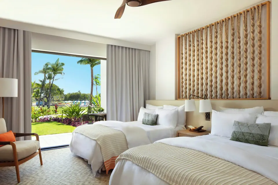 Garden View two-bed room at Mauna Lani with carved wall art and an open view to palms and lawn.