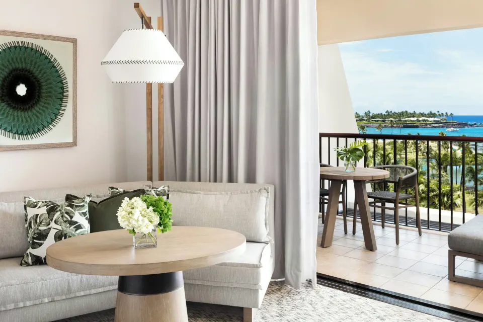 Ocean View room at Mauna Lani with sofa, round table, and balcony overlooking blue ocean water.