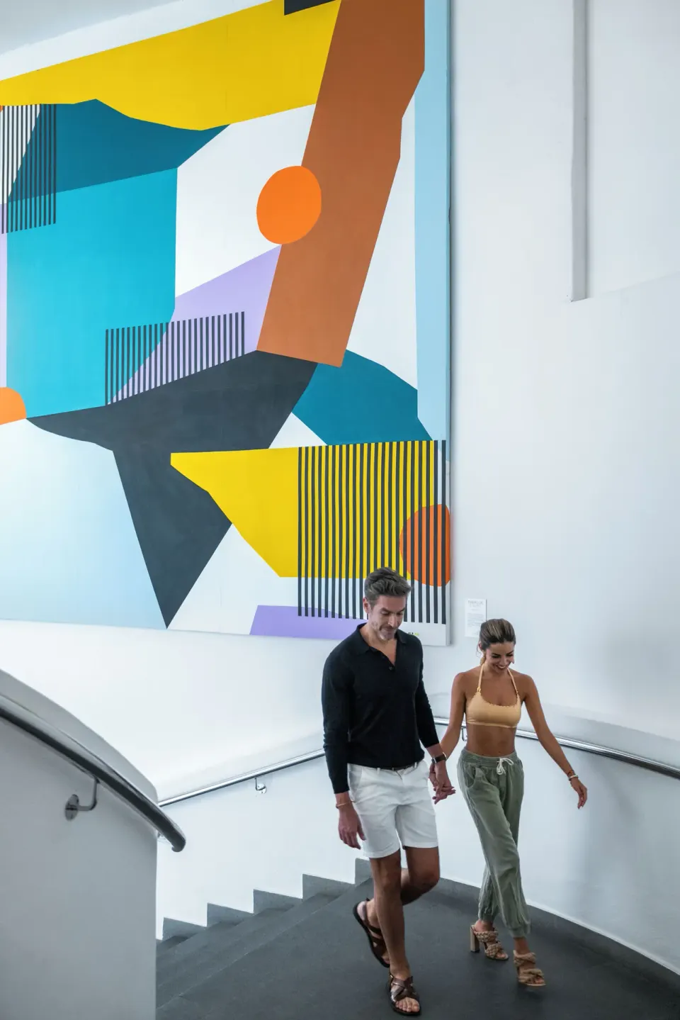 A couple descends a stairway beneath a large abstract painting at ME Cabo.