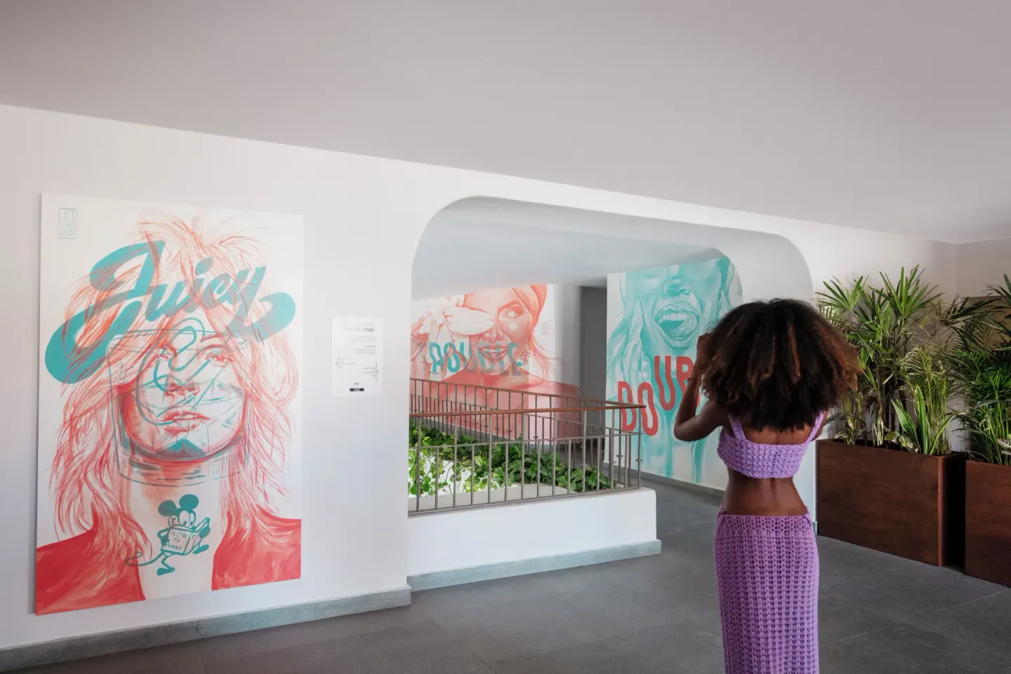 A guest walks through a corridor with colorful portrait murals at ME Cabo.