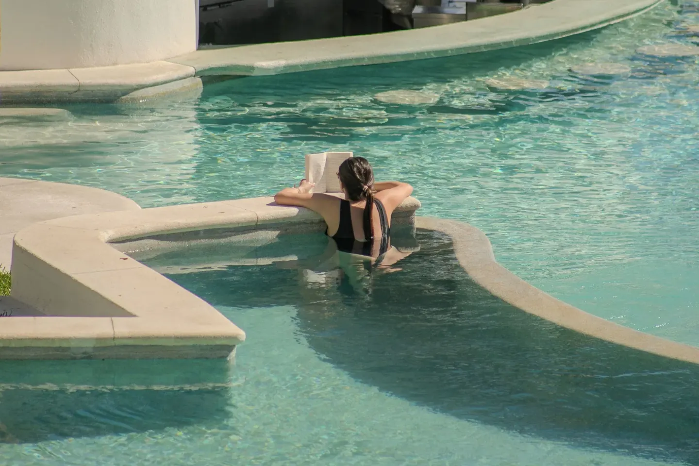 Guest reading at a curved pool ledge in clear water at ME Cabo.