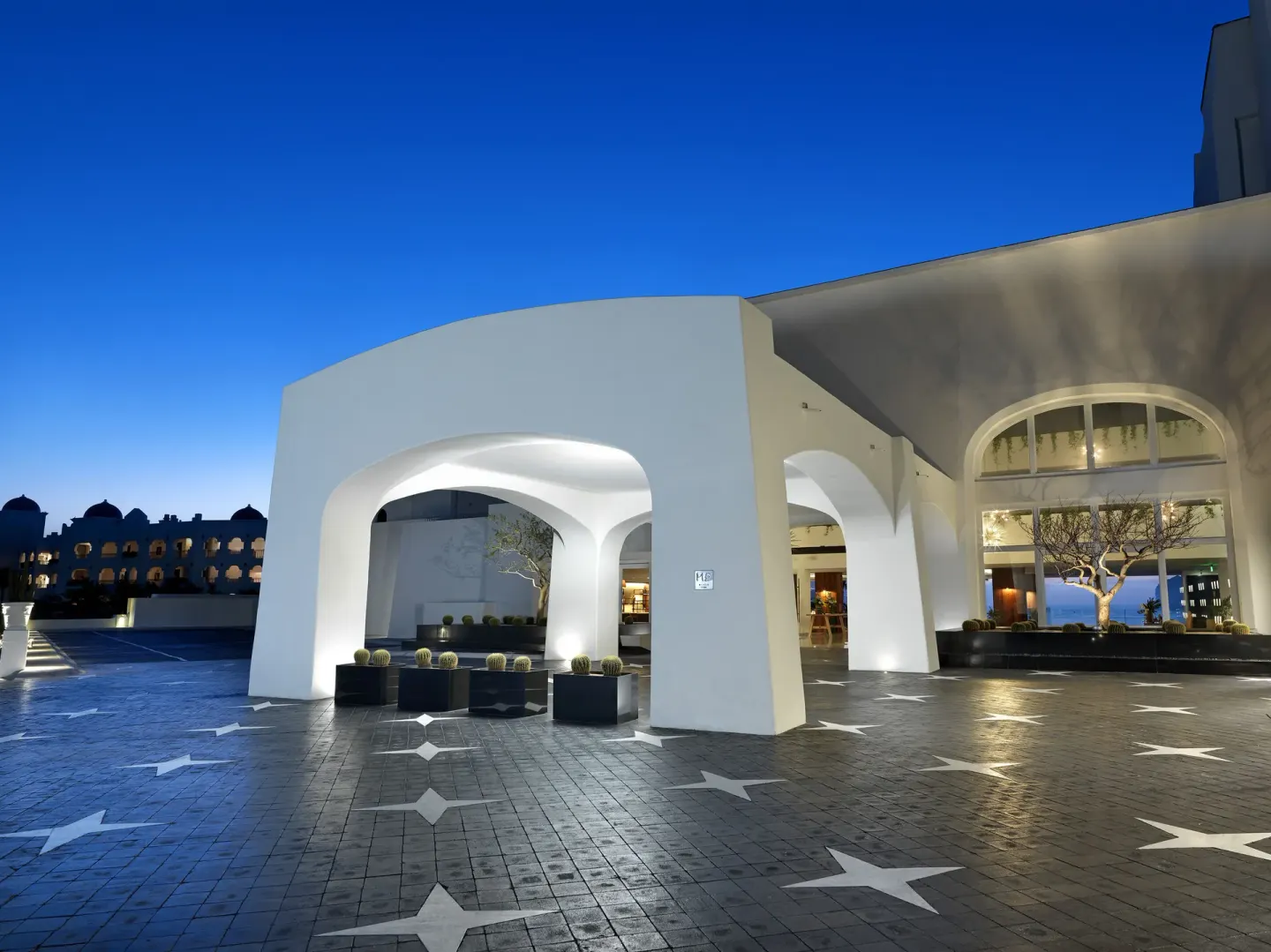 The illuminated white entrance arches and patterned driveway at ME Cabo at dusk.