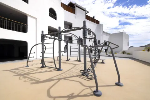 Outdoor exercise rig on a sunny terrace beside the resort building at ME Cabo.