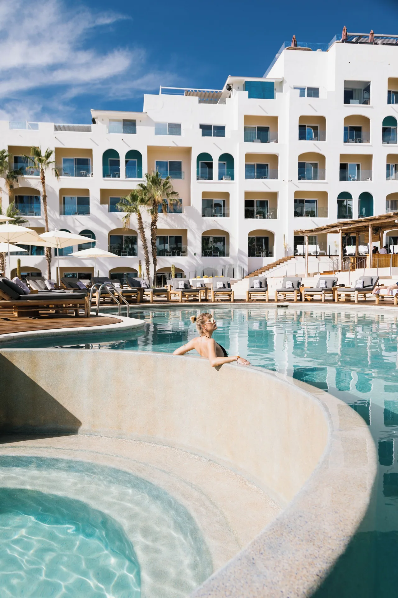 A guest relaxes in the pool below the white guestroom building at ME Cabo.