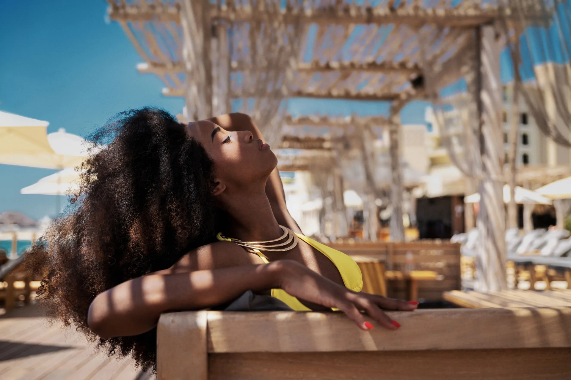 A guest relaxes on a cushioned lounger beneath a wood pergola at ME Cabo.