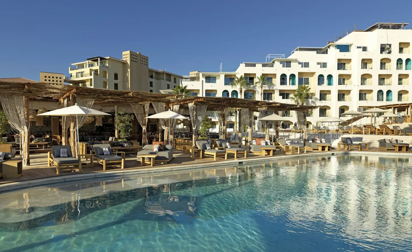 Poolside loungers and shaded cabanas beside the resort building at ME Cabo.
