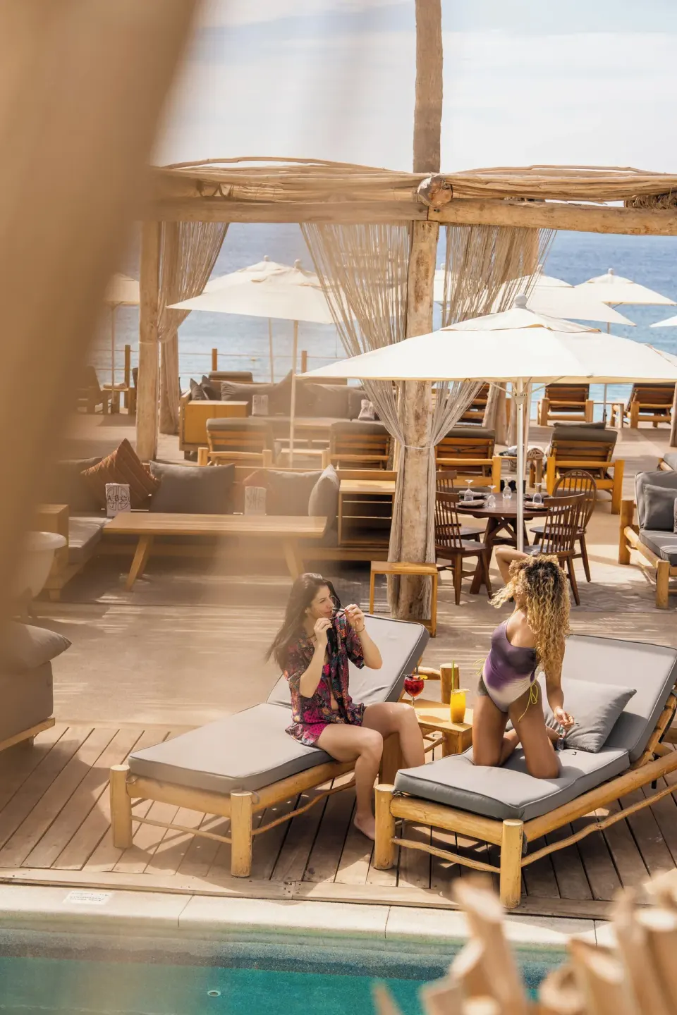 Guests reclining on poolside loungers with oceanfront seating behind them at ME Cabo.