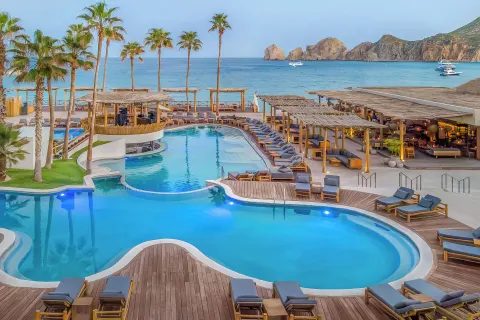 Curved resort pools, loungers, palm trees, and ocean views at ME Cabo.