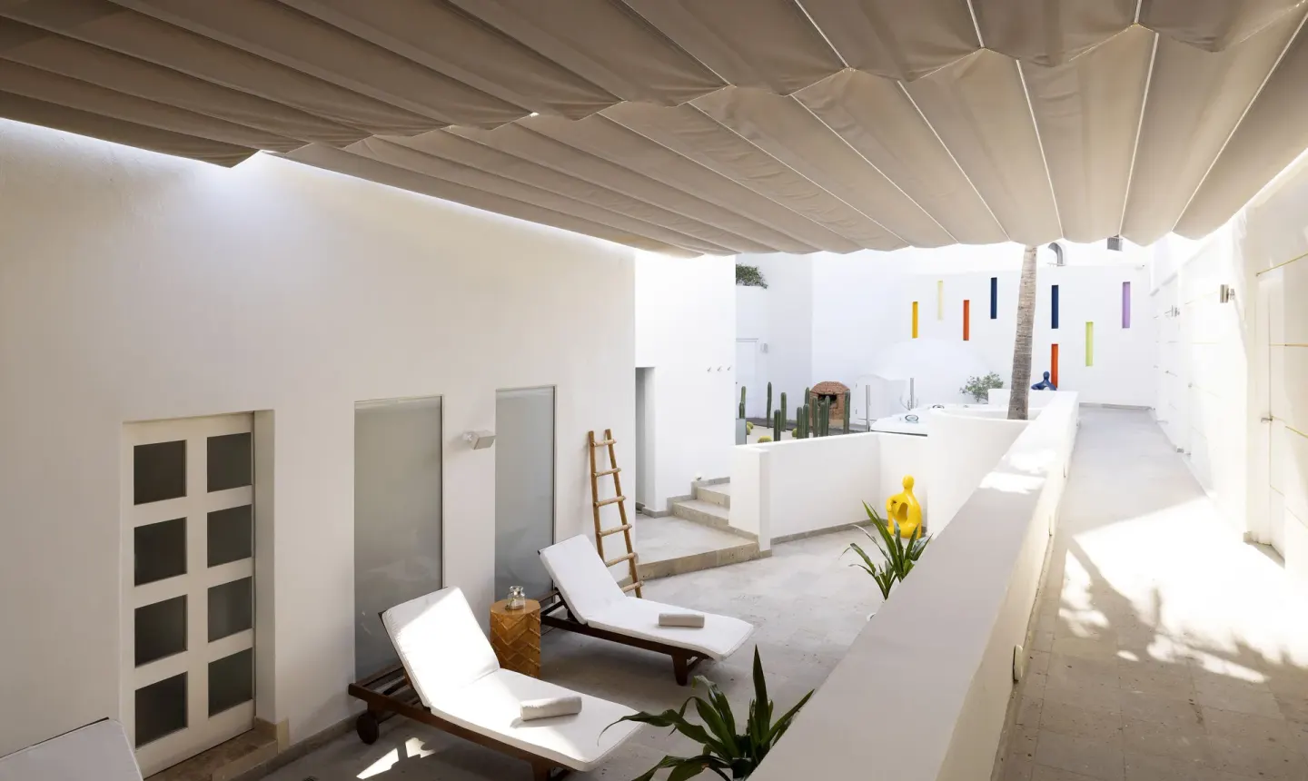 Shaded white courtyard with loungers and sculptural accents at ME Cabo.