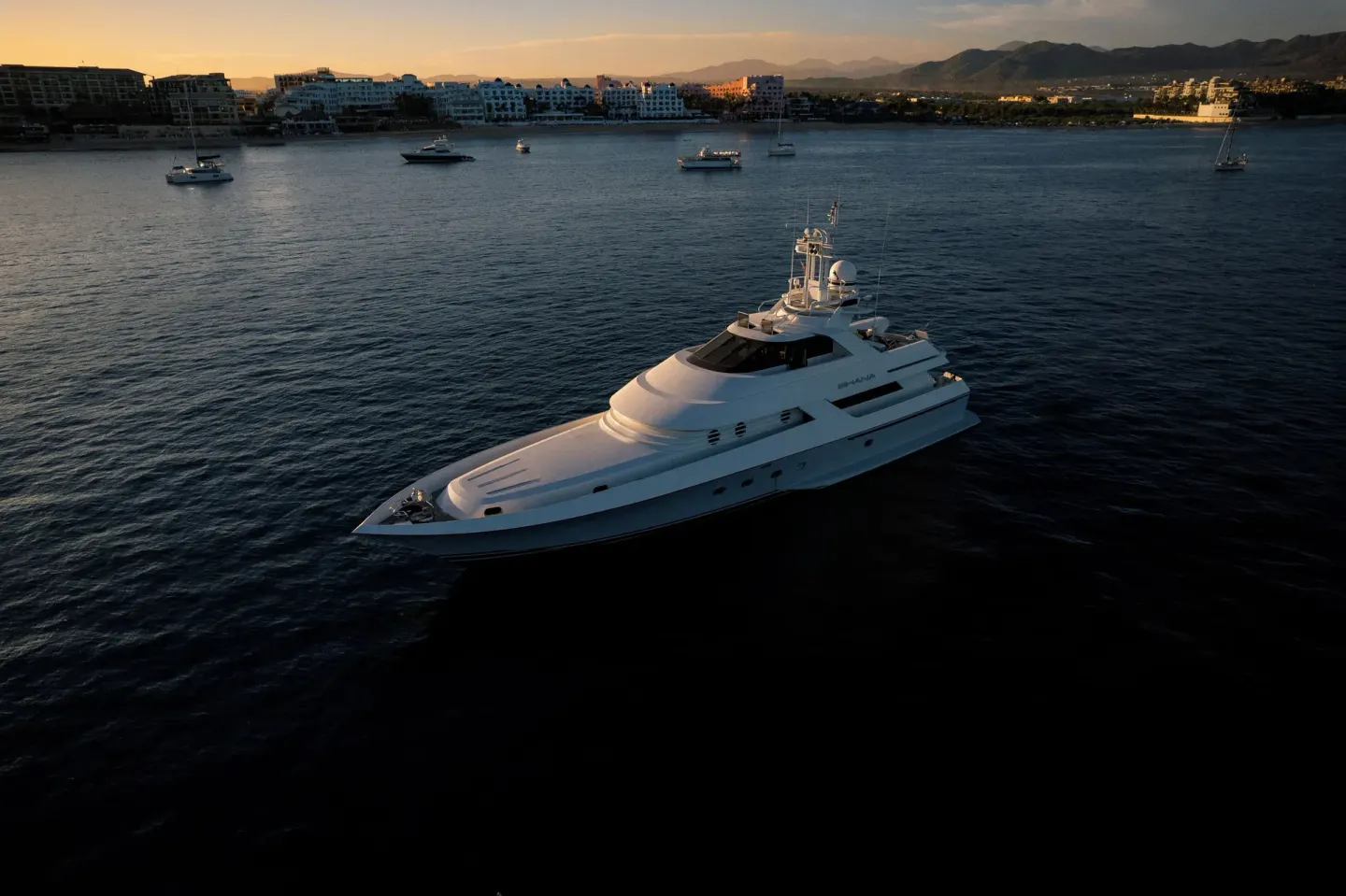 Yacht on the water at sunset near ME Cabo, with shoreline and mountains beyond.