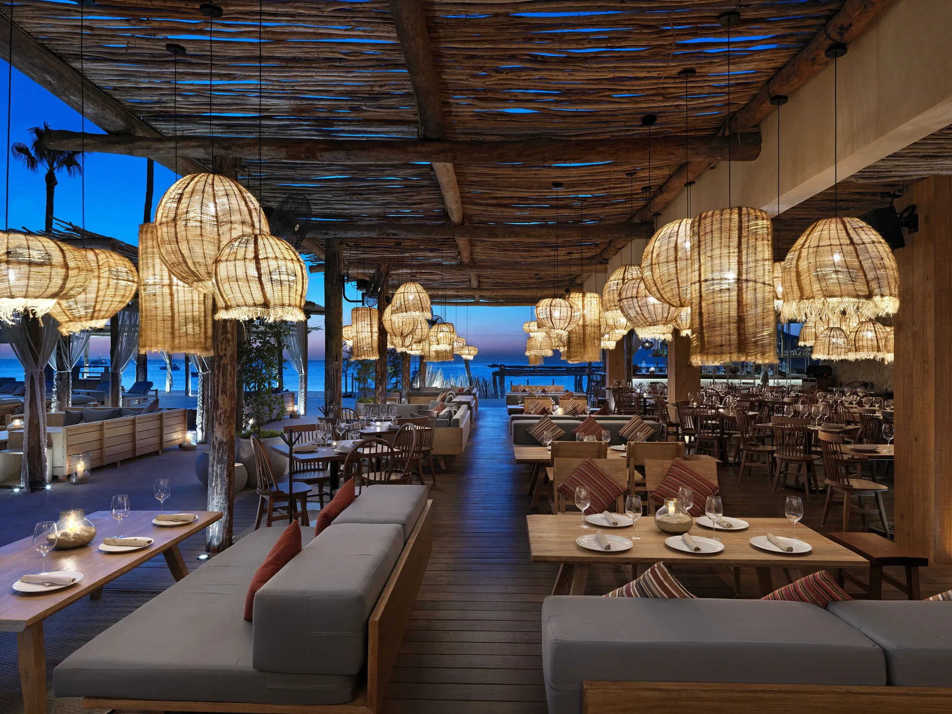 A warmly lit beachside dining room with woven lamps and ocean views at ME Cabo.