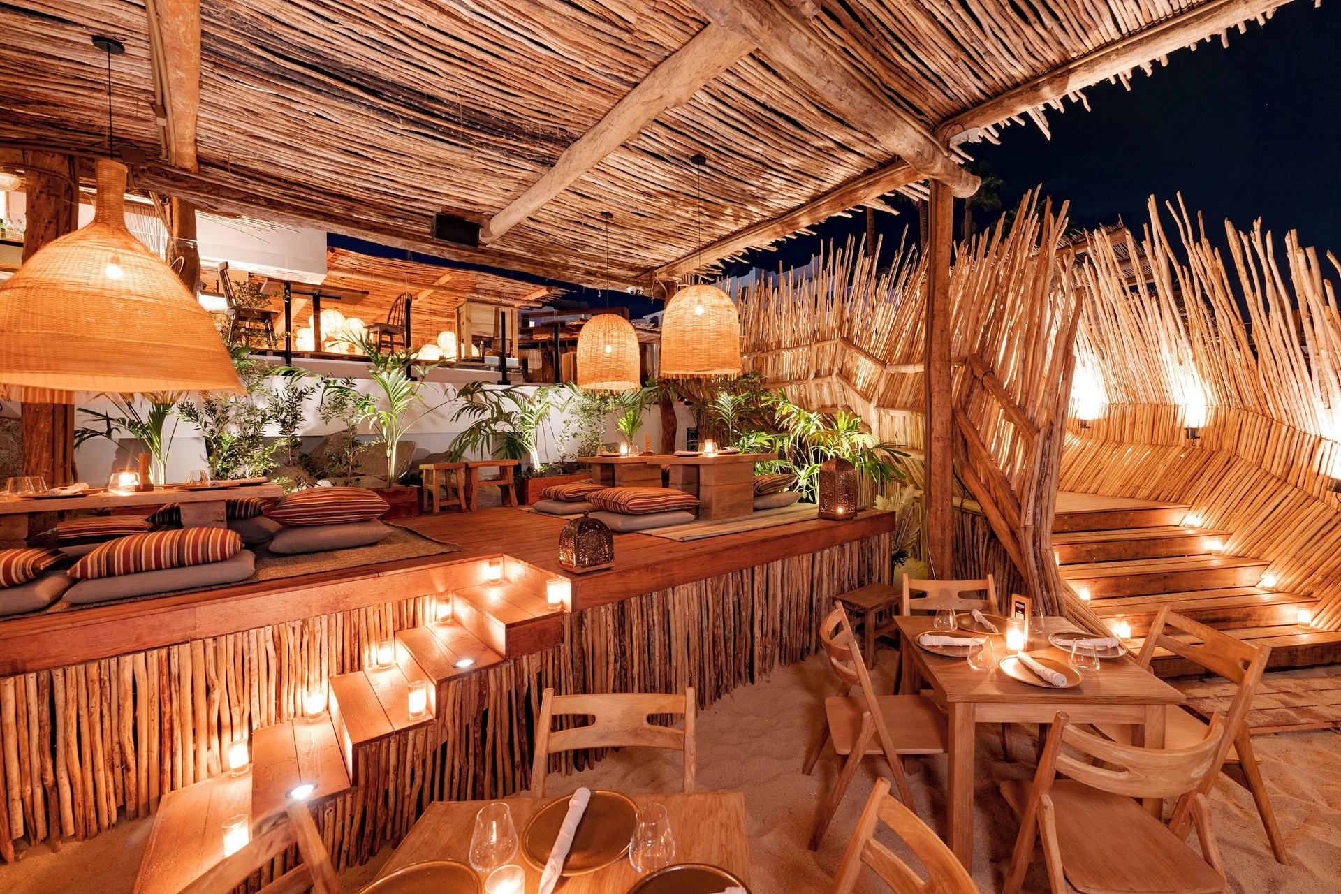 Candlelit Funky Geisha dining area with low cushions and wood tables at ME Cabo.