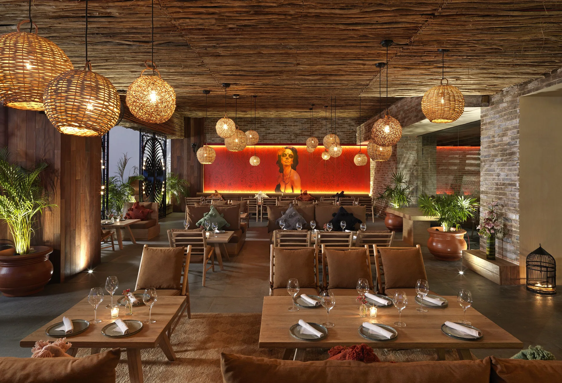 A restaurant dining room with wicker lights, plants, and a red feature wall at ME Cabo.