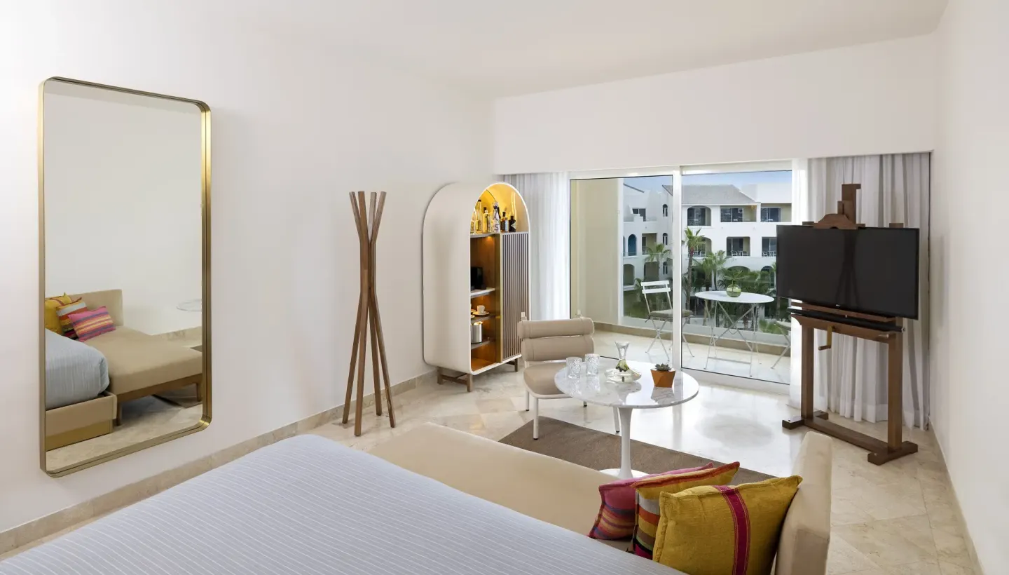 Guest room with king bed, lounge area, TV, and balcony at ME Cabo.