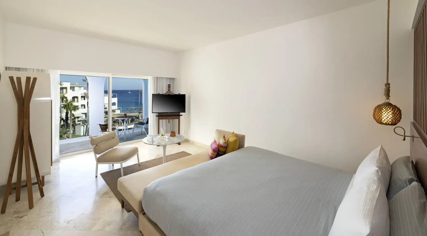 Guest room with king bed, seating area, balcony, and ocean view at ME Cabo.