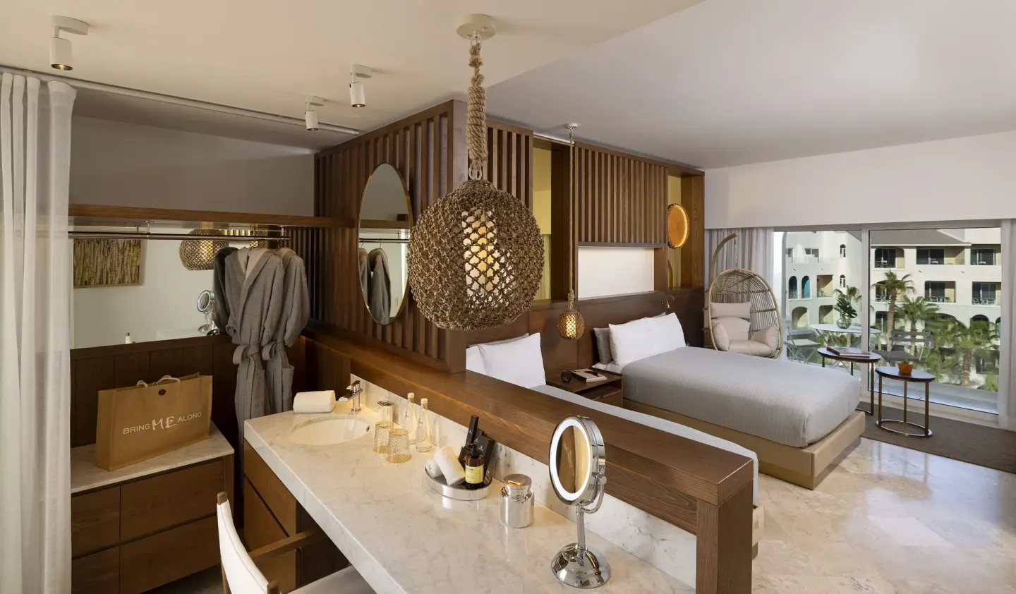 Superior ME+ king bed room at ME Cabo with vanity, wardrobe, hanging chair and balcony windows.