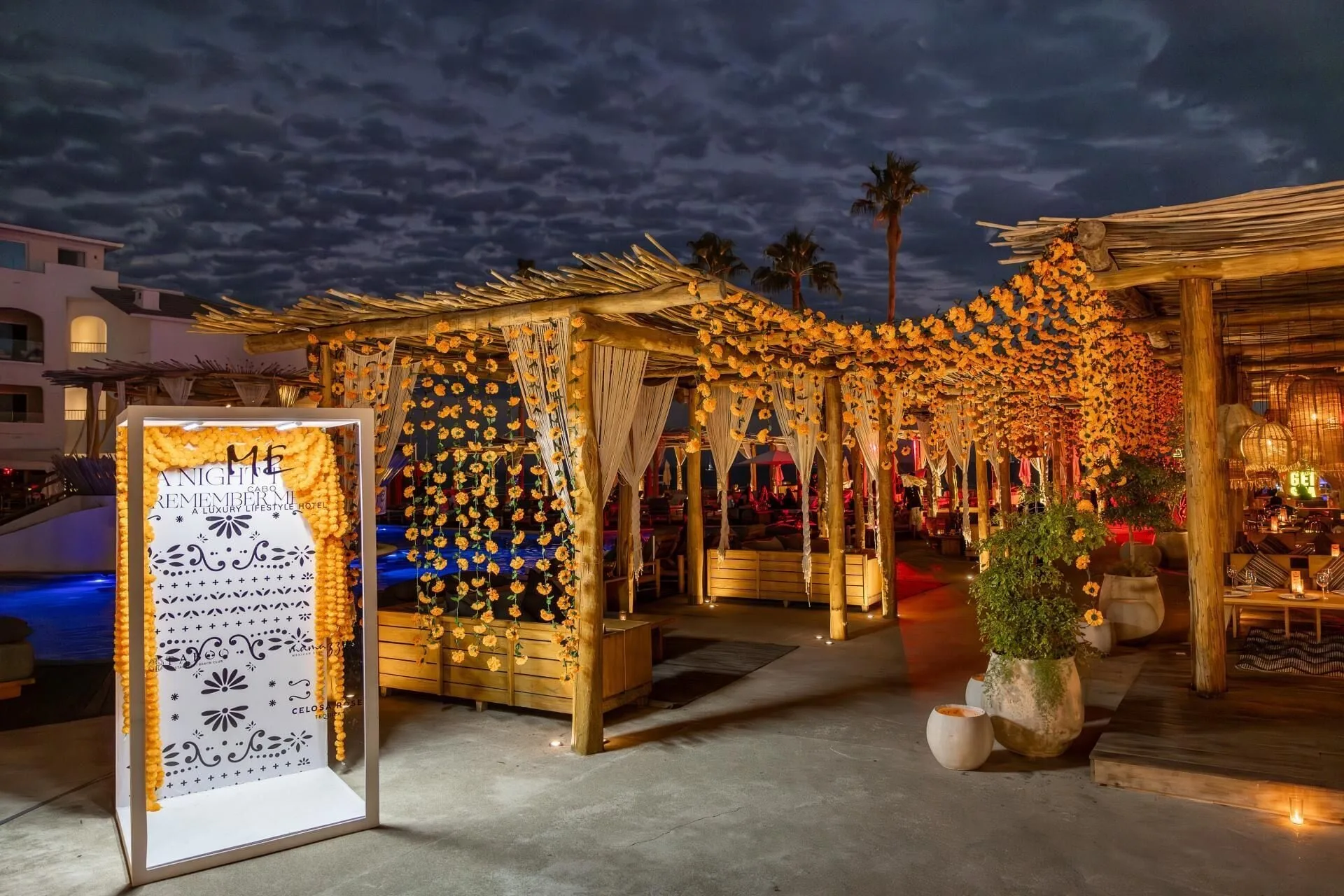 A flower-draped outdoor walkway glows at night during an event at ME Cabo.