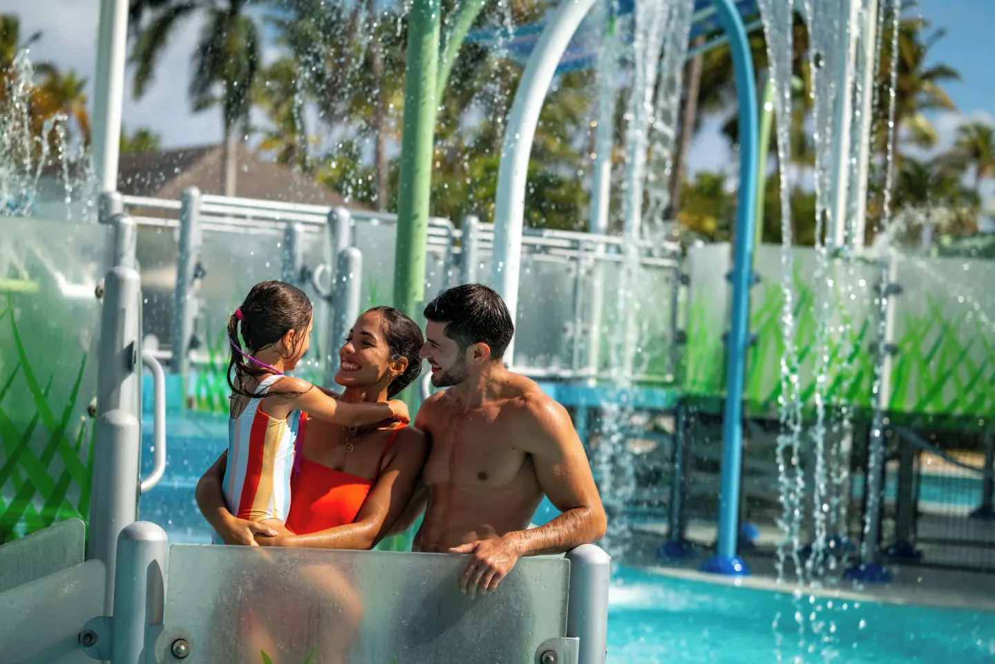 Family smiling beneath falling water in the aqua park at Melia Caribe Beach Resort.