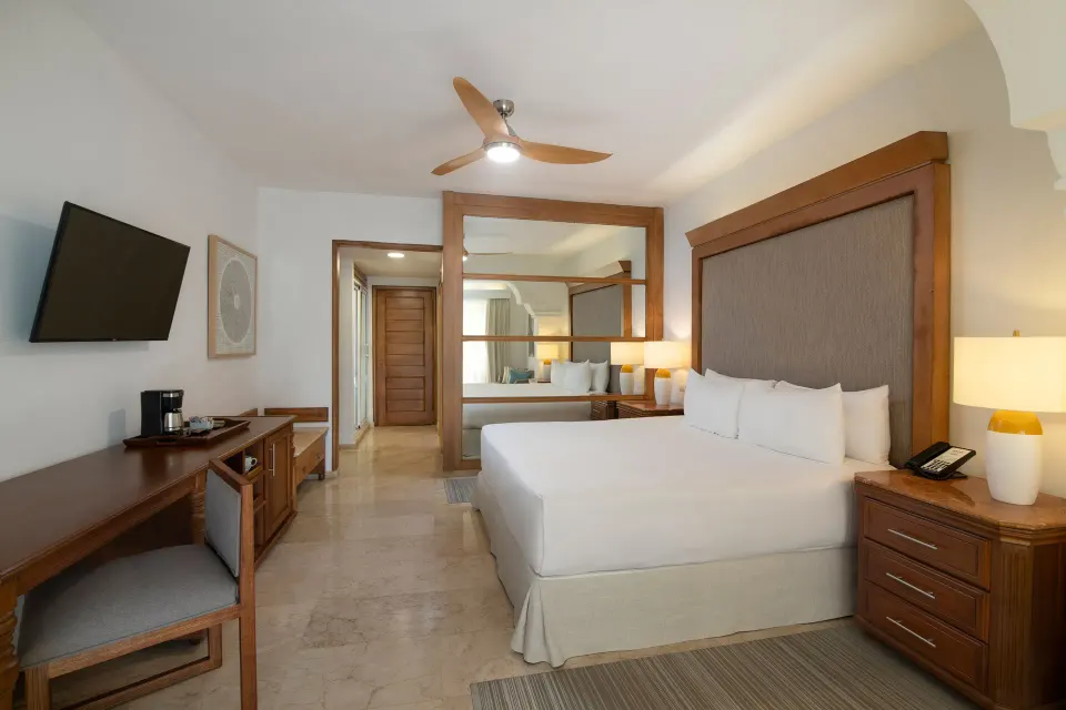 King bed with wall-mounted TV and wood desk in The Level Junior Suite Garden View at Melia Caribe Beach Resort.