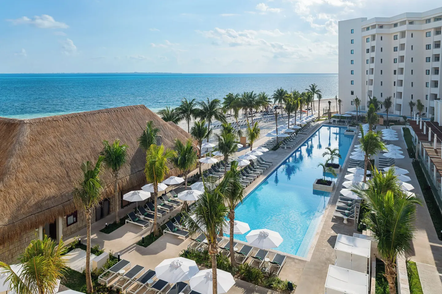 Aerial view of the pool, palms, palapa roof and ocean at Melia Casa Maya Cancun.