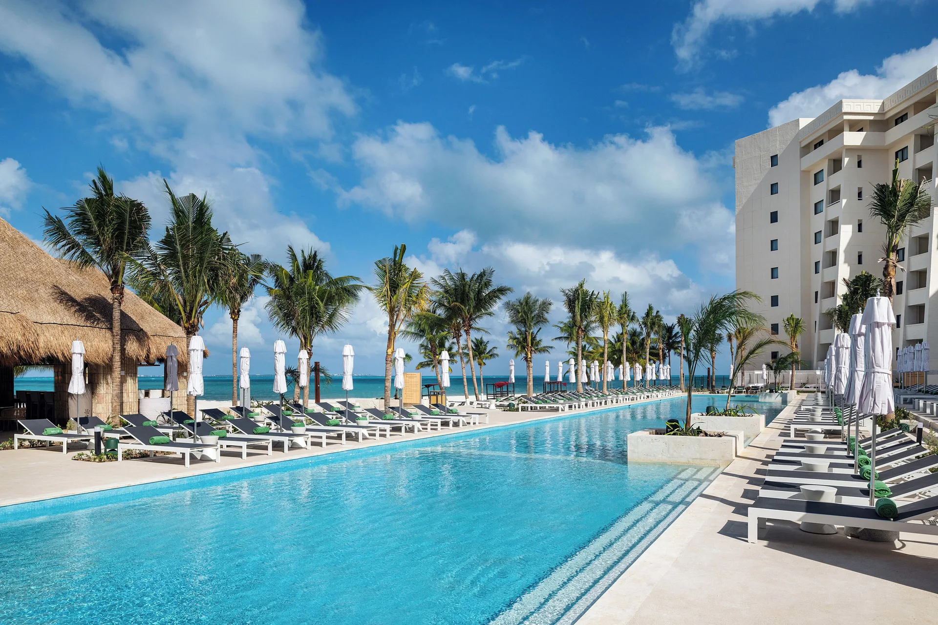 Long resort pool lined with loungers, umbrellas and palms at Melia Casa Maya Cancun.